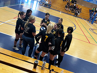 Volleyball team in a huddle with coach on the court